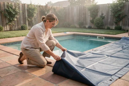 Femme installant une bâche solaire bleue sur une piscine rectangulaire dans un jardin résidentiel